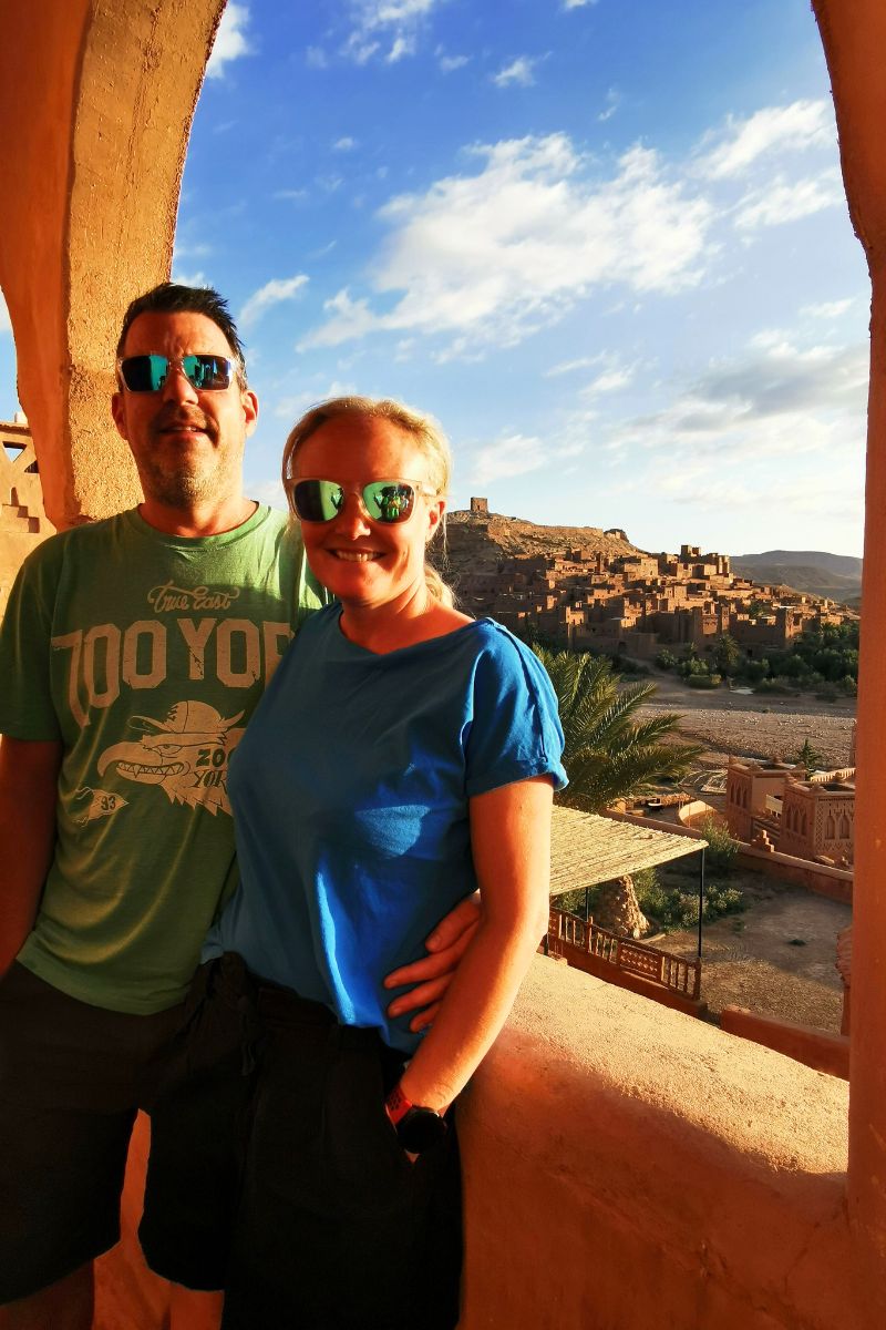 Couple standing in an archway view a view of Ait-Ben-Haddou in Morocco in the background.