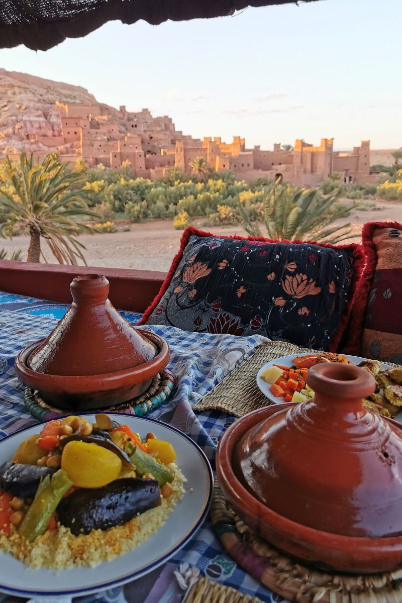 Tagines on a table in a restaurant with a view of Ait Benhaddou in the background.