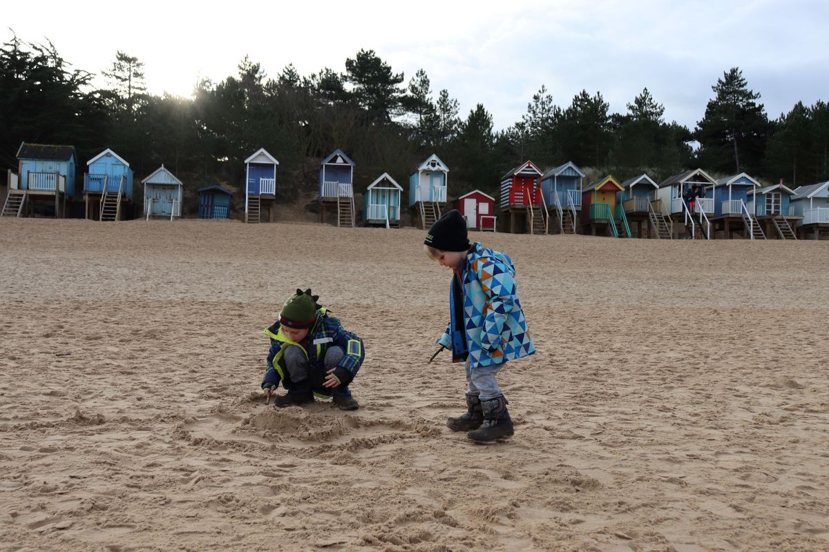 Kids on Wells-next-the-sea beach with lots of colourful beach huts in the background.