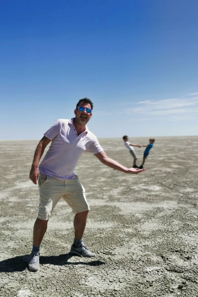 Man using trick photography to hold kids in his hand on the salt pan in Etosha National Park.